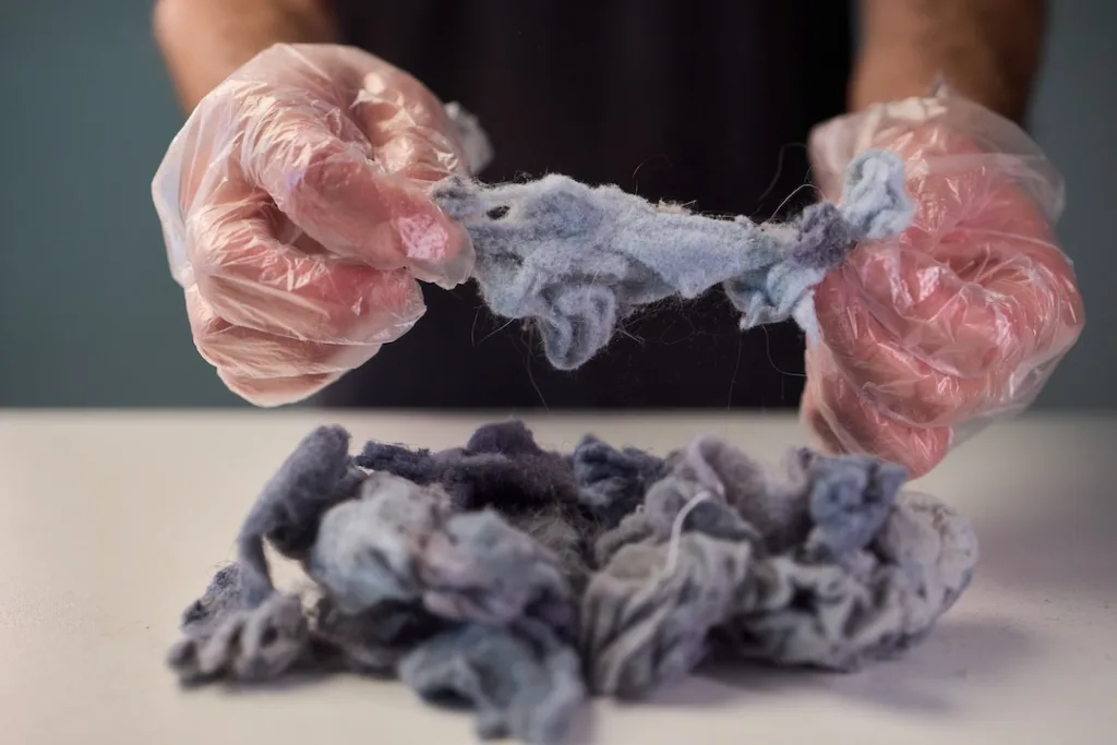 hands holding dryer lint closeup, fluffy gray fibers pulled from lint trap filter, bare palms inspecting debris, textured soft fuzz, natural window light,