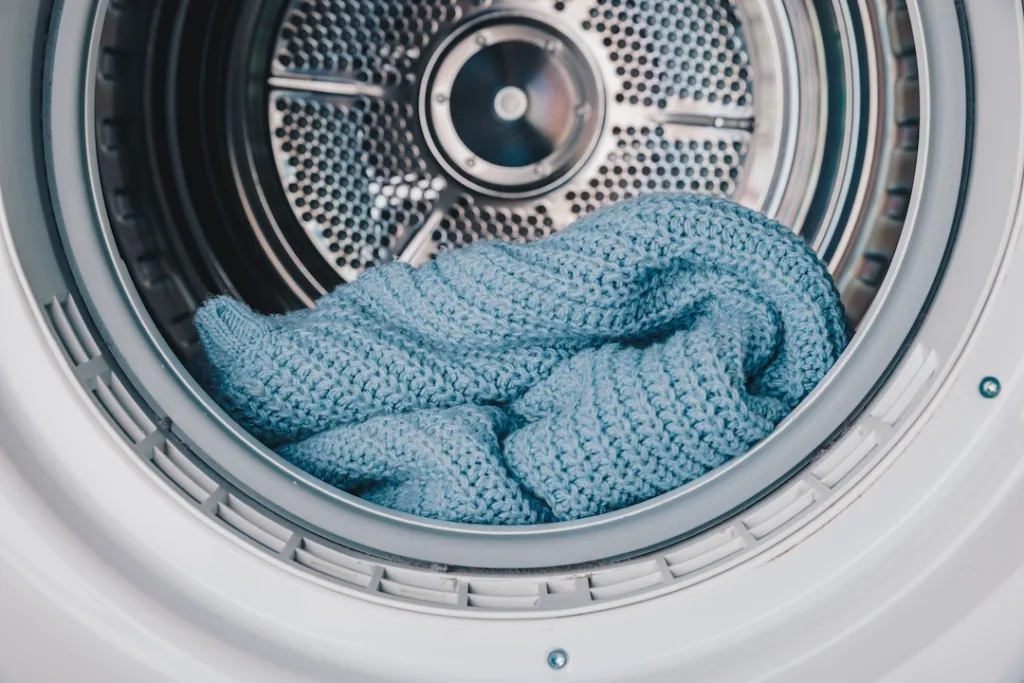 Close-Up View of a Cozy Blue Knitted Blanket Inside a Modern Washing Machine Drum or Clothes Dryer, Highlighting Soft Textures and Efficient Laundry Care
